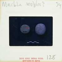 The image is a photograph of two marble weights on a scale, with the focus being on the right weight which appears to be heavier or denser than the left one.