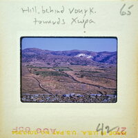 A vintage photograph of a mountainous landscape with terraced fields and a village below.