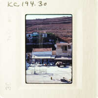 Photo depicts a rural village scene with buildings and vehicles, taken from an elevated perspective.