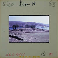 A vintage photo of a hilly landscape with trees and water, marked as "site from N" on an old film strip.