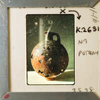 An old, weathered clay pot with a handle and an opening at the top.