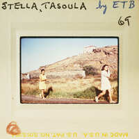 Two women walking on a road with mountains in the background.