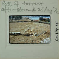 A photograph of a barren landscape with stone walls and a body of water, possibly the sea, in the background.