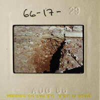 A photograph depicting an outdoor scene with a large crack in a building, possibly a bridge or wall, and a close-up of the ground showing a dirt path.