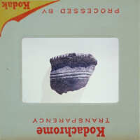 Small, dark-colored artifact with a rough texture and visible lines or patterns on it.