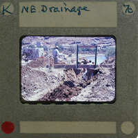 Picture of a man working on a drainage ditch with mountains in the background, taken from an old film negative.