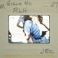 A man bent over, working on a rock or digging with a pickaxe.