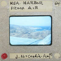 Aerial photograph of a harbor with mountains and water, taken from an airplane window.