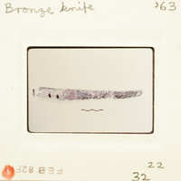 Old photograph of an ancient bronze knife with visible patina and signs of wear.