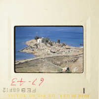 A photograph of an island with a church and houses, taken from a distance, showing a clear sky and calm sea.