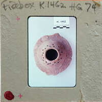 A small, round clay object (K.1462) with a hole in the center and multiple holes around its circumference.