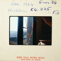 A photograph of an antique necklace with red beads and a gold clasp, displayed against a window view.