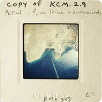 Aerial view of coastline with blue water and brown land, captured on an old photograph.