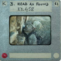 Close up of terracotta figurine face next to stone wall.