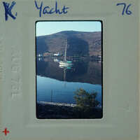 Old photograph of a boat on calm water with mountains in the background, enclosed in a vintage film strip holder.