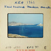 View of coastline with blue water and distant mountains, captured on an old photograph.