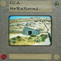 A photograph of a small stone building with mountains in the background, presented on a faux film strip.