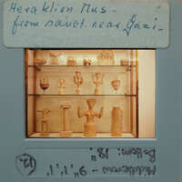 Ancient figurines displayed on shelves inside a case, with labels indicating their origin.