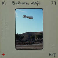 A large white balloon floating above a landscape with mountains and trees.