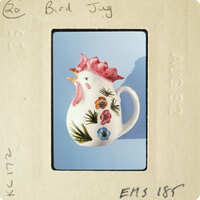 A ceramic rooster mug with colorful flowers and leaves painted on it.