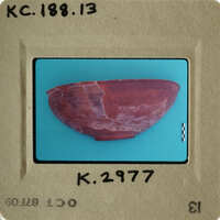 Ancient red clay bowl with cracks and imperfections, photographed on a blue background.