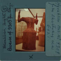 Image of a clay sculpture on display, with handwritten notes and numbers on the border.