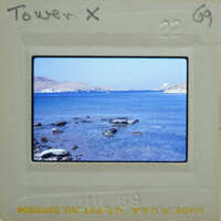 Picture of a serene beach with calm waters and distant mountains, taken on film.