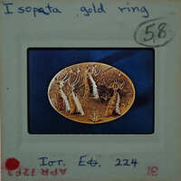 Gold ring with intricate design, possibly depicting a scene or figures, set against a blue background.