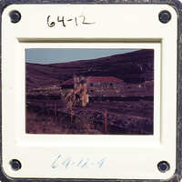 A photograph showing a rural landscape with buildings and vegetation, framed by an old slide mount.