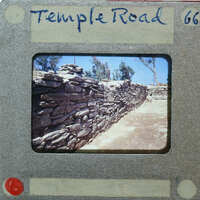 Stone wall with vegetation on top, set against a clear sky.