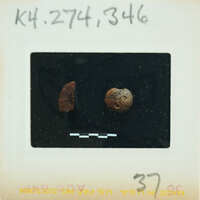 A photograph of a small, round object with markings on it, possibly an artifact or a coin, placed against a dark background.