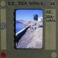 A vintage film strip with a photo of a coastal scene, including a stone wall and water.
