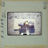 A photograph of two rocks on a surface with a shadow cast by the photographer's hand.