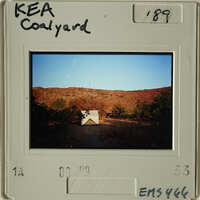 A photograph of a house on a hillside with trees and shrubs, taken during sunset.