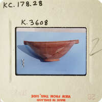 A photograph of an ancient ceramic bowl with visible cracks and imperfections, displayed on a blue surface.