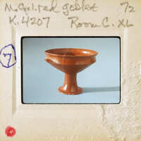 An old brown ceramic bowl with a handle on display.