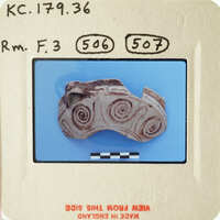 Ancient artifact with spiral designs on a blue background, photographed and labeled for documentation.