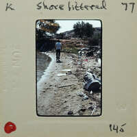 A vintage photograph of a person walking on a beach with litter and debris scattered around.