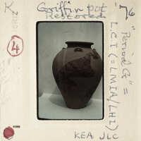 A photograph of a brown vase with markings, displayed on a white surface.