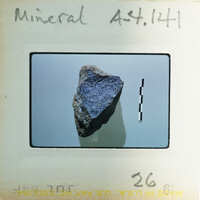 A small, dark blue gemstone on a white surface with black check marks and a label.