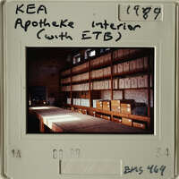 Old photograph of an interior room with shelves filled with boxes and a table in front.