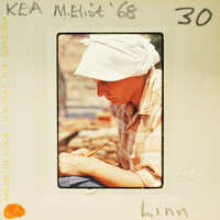 Woman sitting down writing with pencil and paper, wearing a hat.