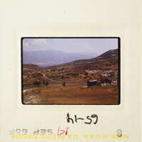 A photograph of a mountainous landscape with a dirt road and sparse vegetation.