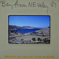 A vintage photograph of a coastal village with mountains and blue water.