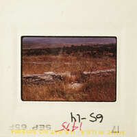 Old photograph of stone ruins with grass and dirt, taken from behind a fence.