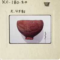 Ancient artifact, possibly pottery, displayed on a white surface with visible cracks and imperfections.