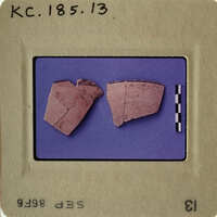 Two broken pottery shards on blue background with white border, labeled "KC.1856.13".