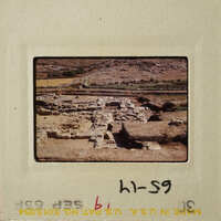 Ancient ruins with stone walls and pathways, set against a backdrop of arid landscape.