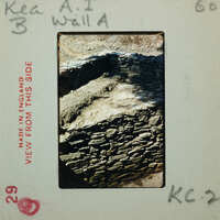 Old stone wall with surface and vegetation towards the top.