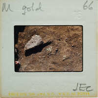 A vintage photograph of a rock on dirt ground with handwritten notes and numbers on the border.